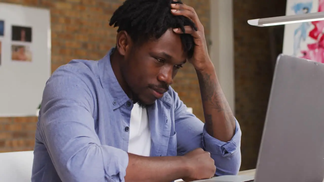 Stressed african american male artist looking at his laptop while sitting on his desk at art studio