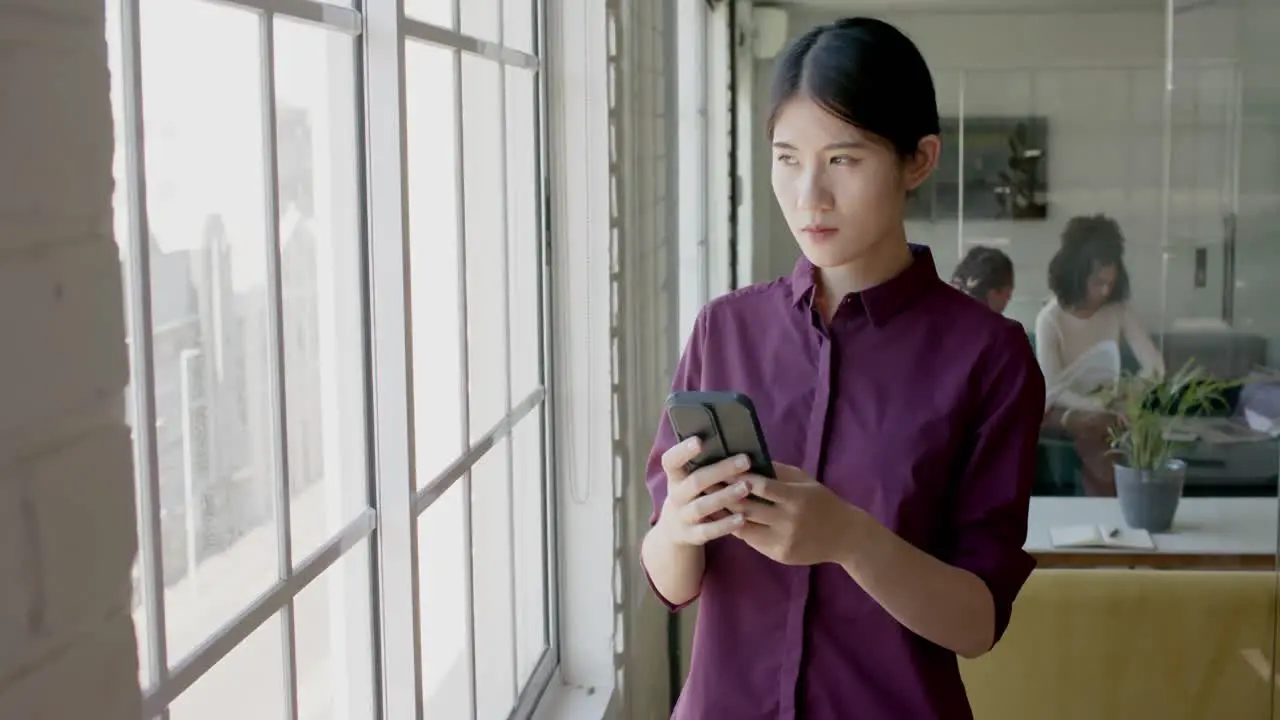 Busy asian casual businesswoman using smartphone in creative office slow motion