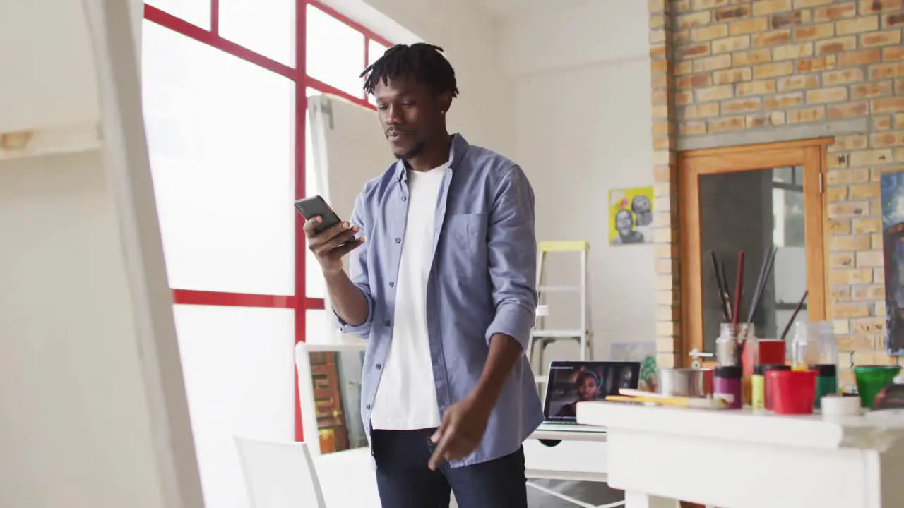 African american male artist taking a picture of a painting with a smartphone at art studio