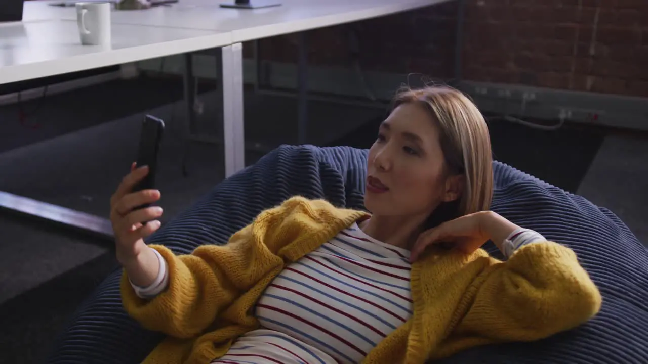 Asian business woman lying on bean bag taking selfie and smiling during break