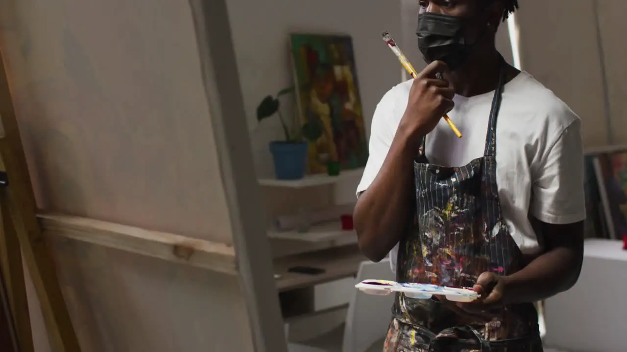 Thoughtful african american male artist holding paint brushes and palette at art studio