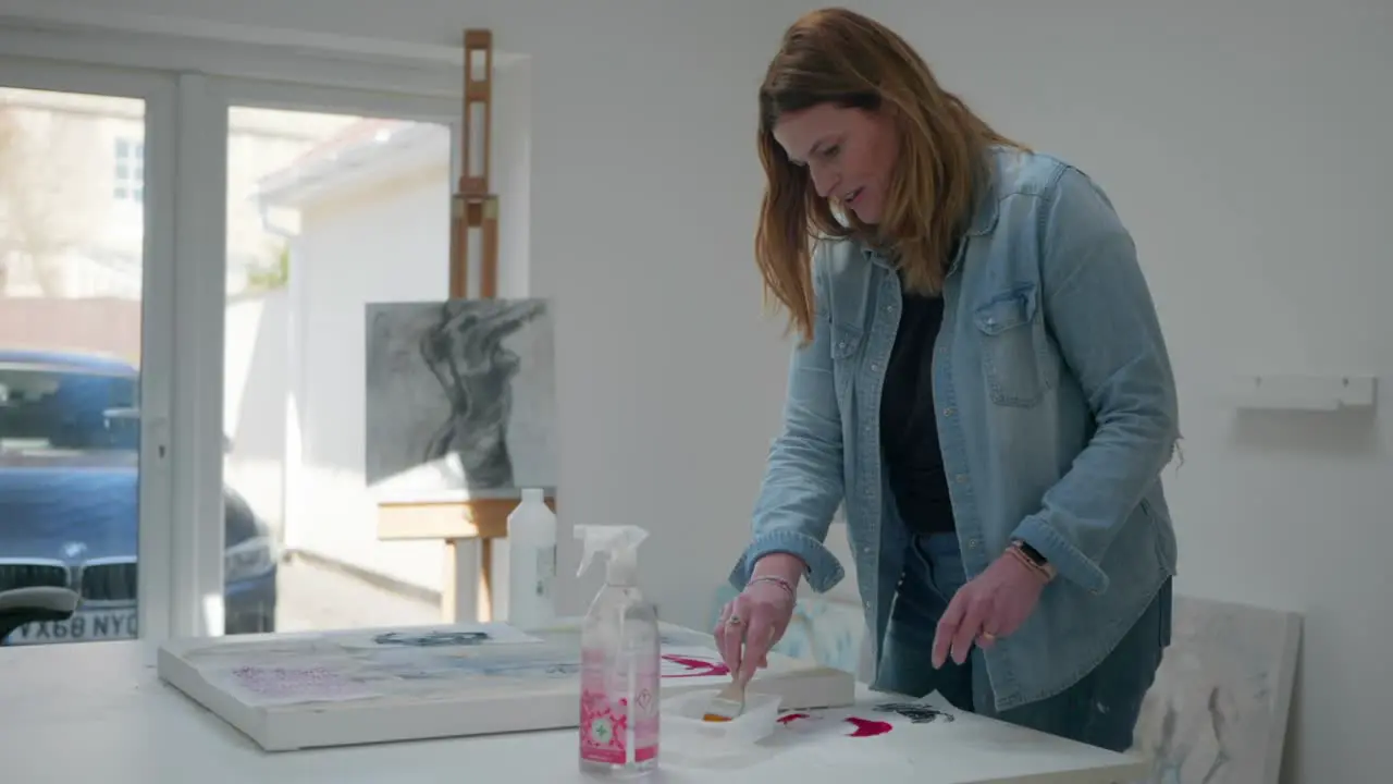 Female artist brushing glue on paper asset on canvas in a home studio