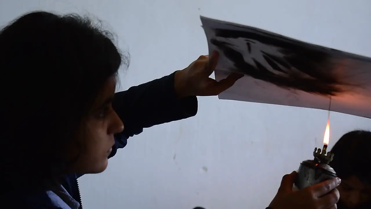 A girl using a candle to create art on a paper at a workshop