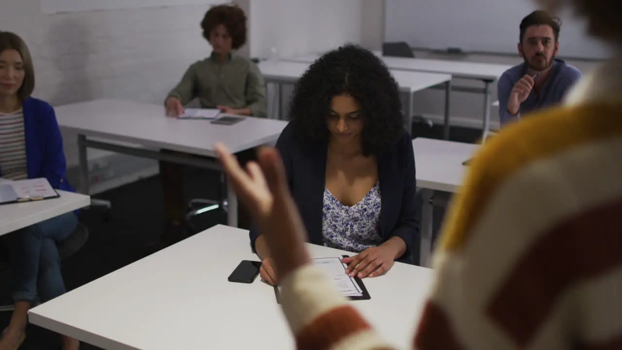 Mixed race colleuagues sitting during presentation in meeting room making notes