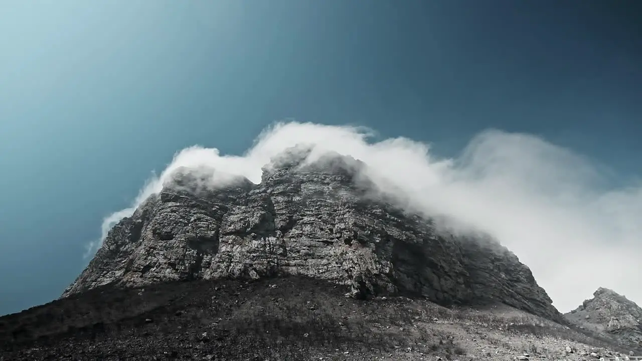 Dramatic clouds move around a huge cliff on Hangklip mountain in South Africa that has burnt down due to wild fires near Pringle Bay