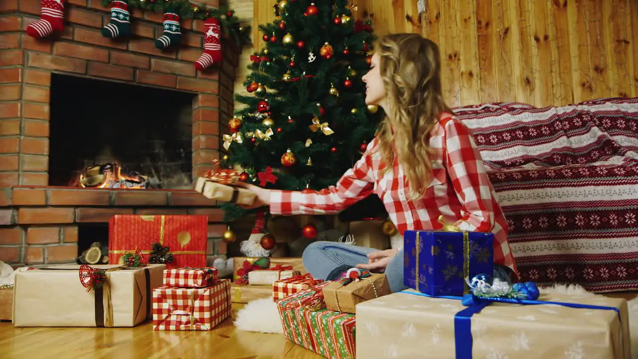 An attractive woman rejoices in New Year's gifts under the tree