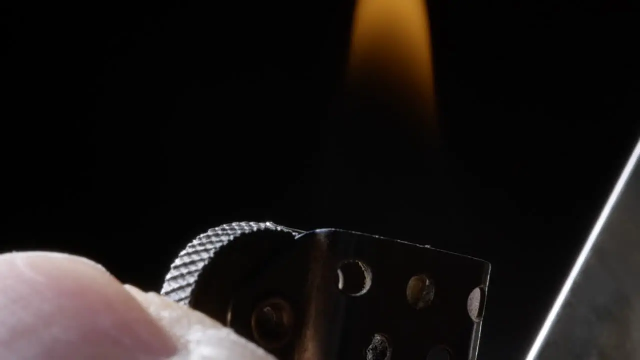 slow-motion close-up of a thumb striking a metal lighter igniting the blue flame