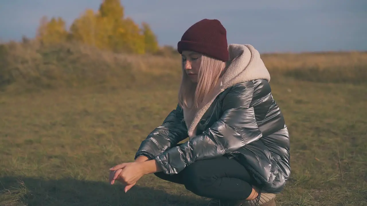 blonde girl in warm jacket heats hands at bonfire in camp