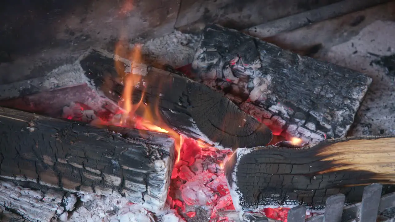 Black charred wooden logs in ash filled fireplace small orange flames