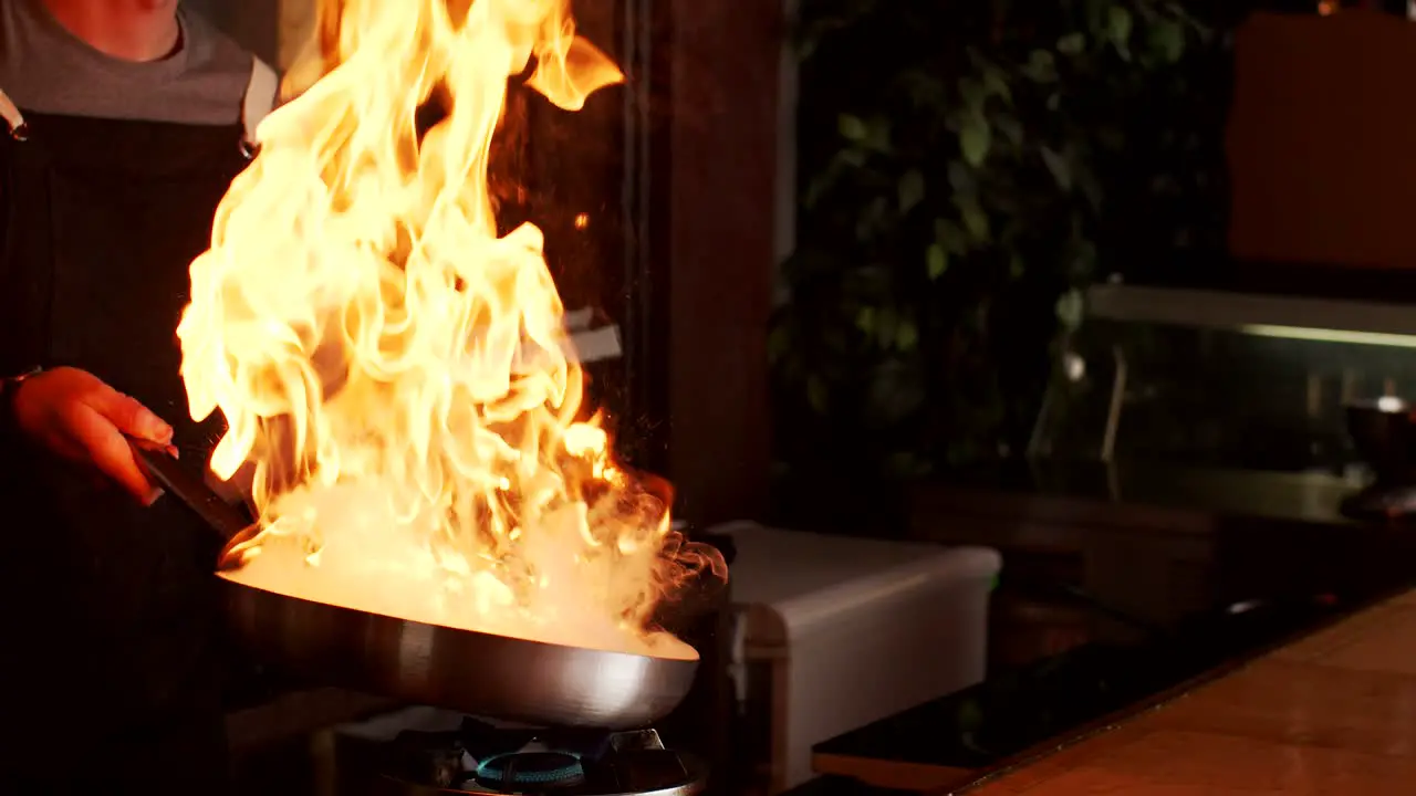 Cook preparing food in frying pan with fire