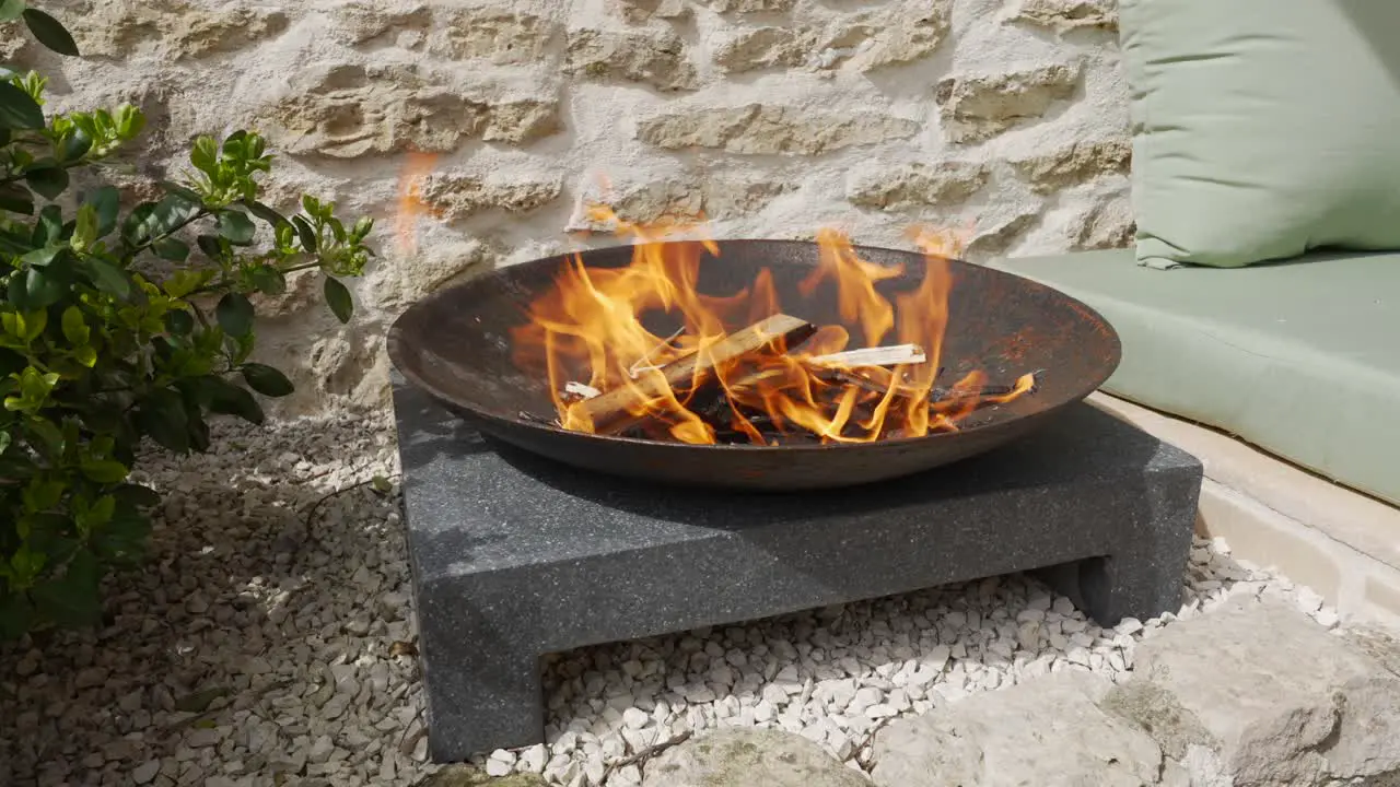 Outdoor fire burns in round cast iron fire pit in a bright sunny day