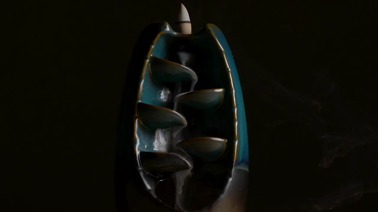 Serene shot of incense flowing over a ceramic holder with black a background