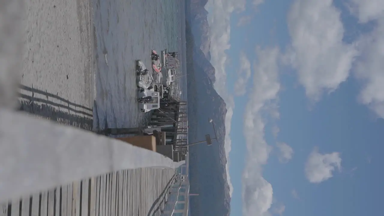 A tranquil wooden pier and boats on a lake with mountains and clouds in the background