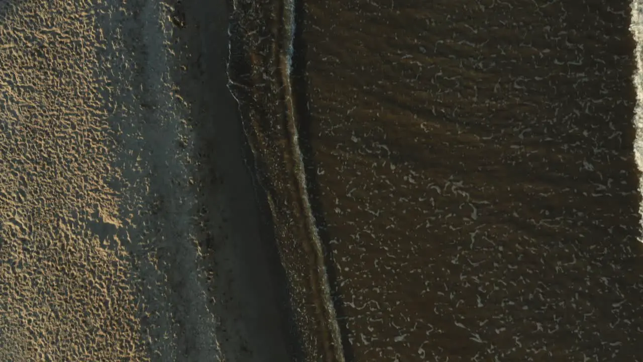 Vertical shot of the beach with small waves colliding at sunset