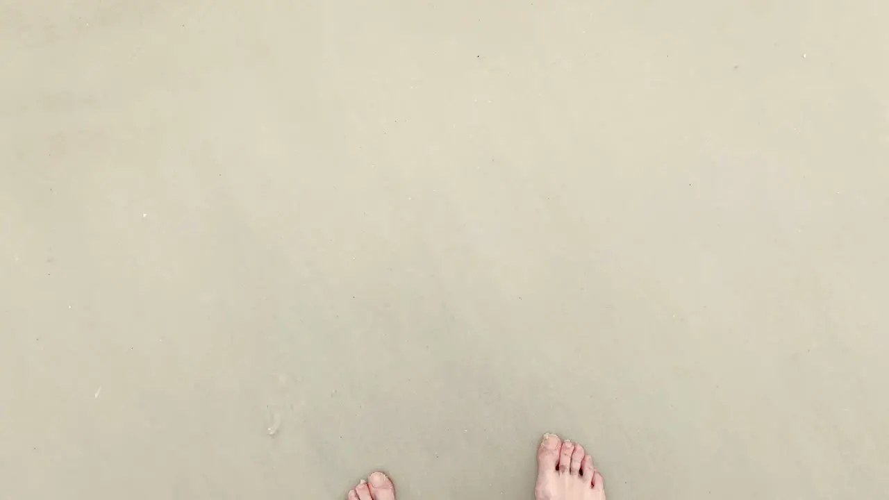 ocean waves wash over beach and feet first person POV