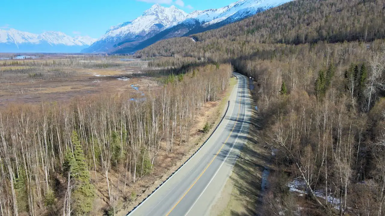 Aerial view of country road with mountains on the right and swamp on the left in the spring prior to the foliage turning green