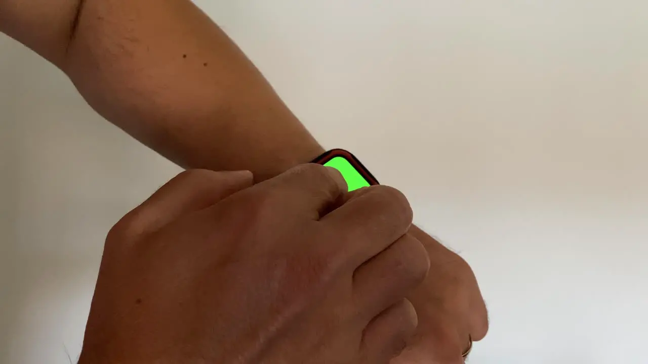 Young male person wearing fitness bracelet with green screen close-up