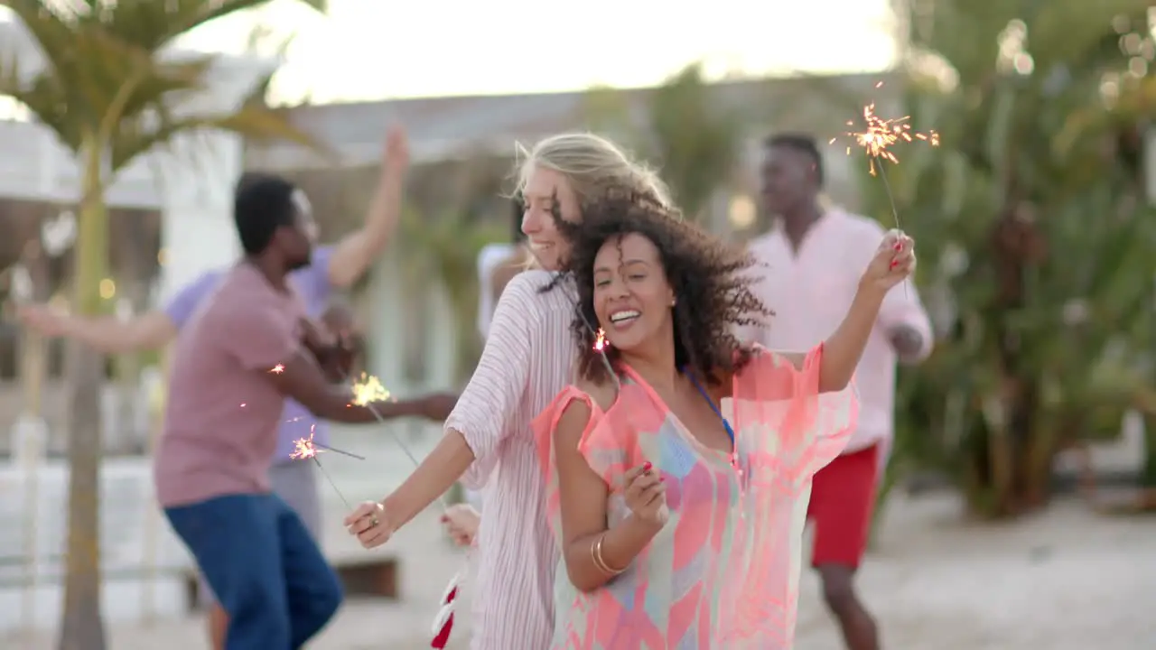 Happy diverse group of friends dancing with sparklers at beach