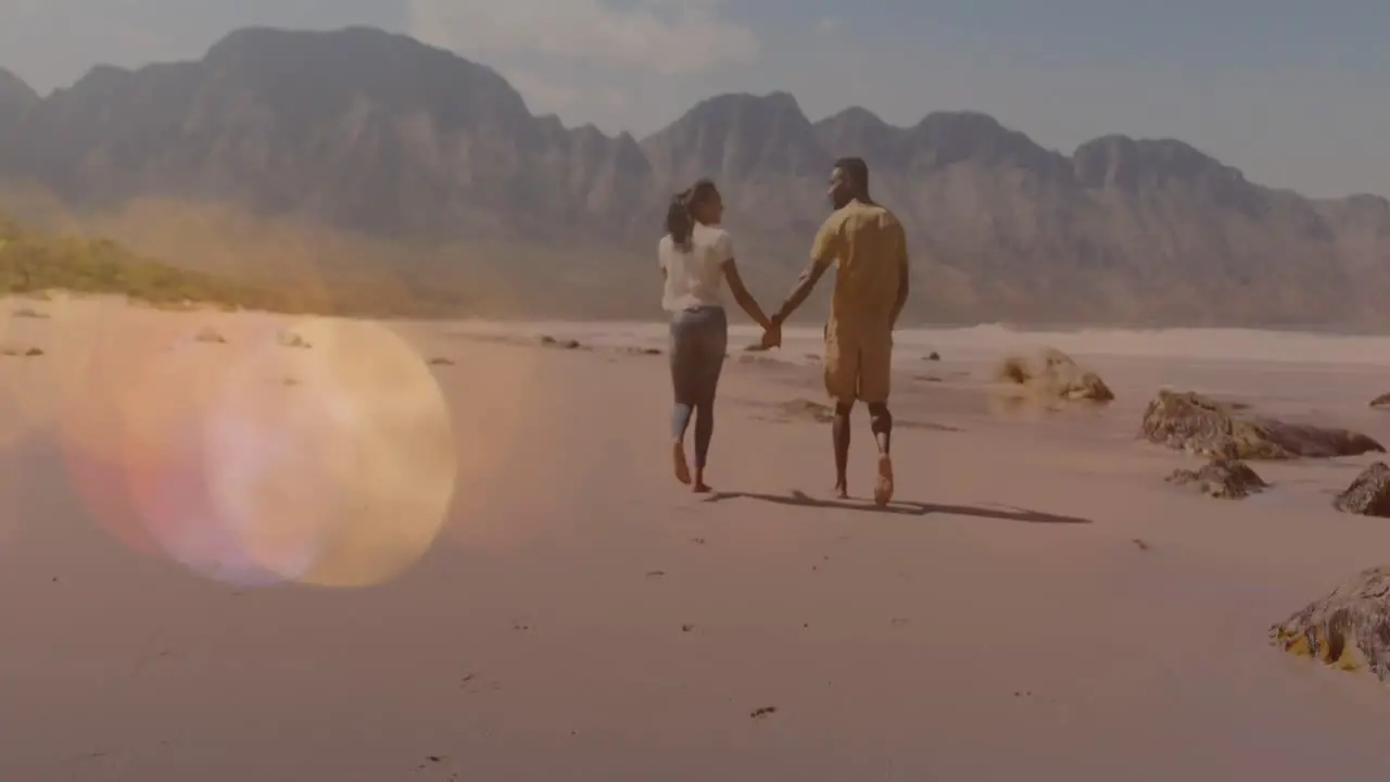 Multiple light spots floating against african american couple holding hands walking at the beach