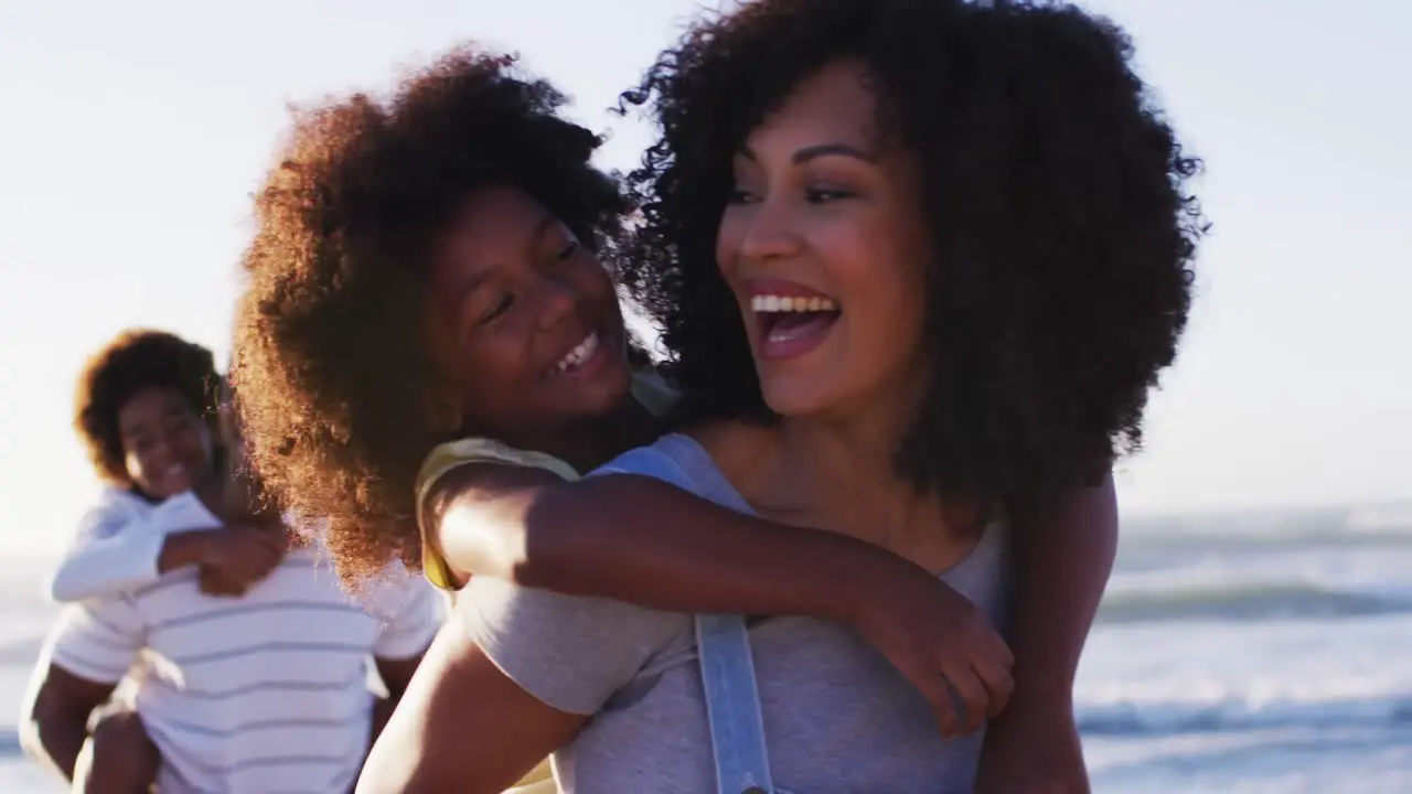 African american mother and father giving a piggyback ride to their daughter and son at the beach