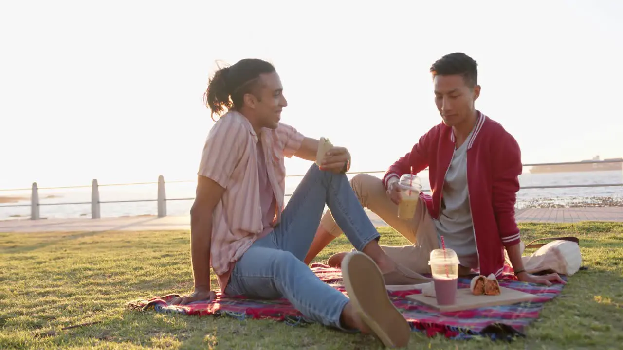 Happy diverse gay male couple having picnic at promenade by the sea slow motion