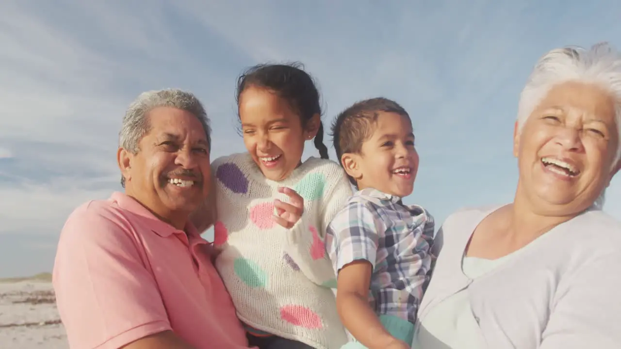 Happy hispanic grandparents and grandchildren having fun on beach at sunset