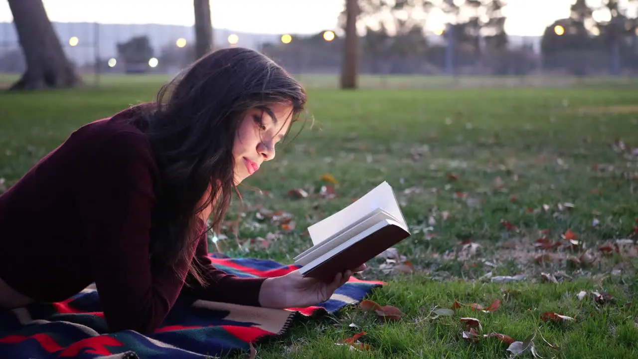 A young hispanic woman reading a book and relaxing in the park at sunset