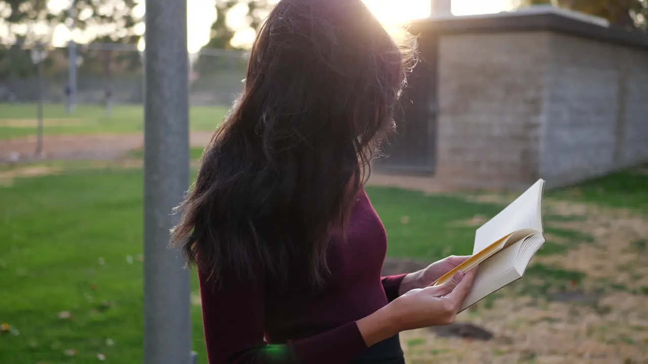 A young woman college student reading a textbook outdoors in the campus park at sunset SLOW MOTION