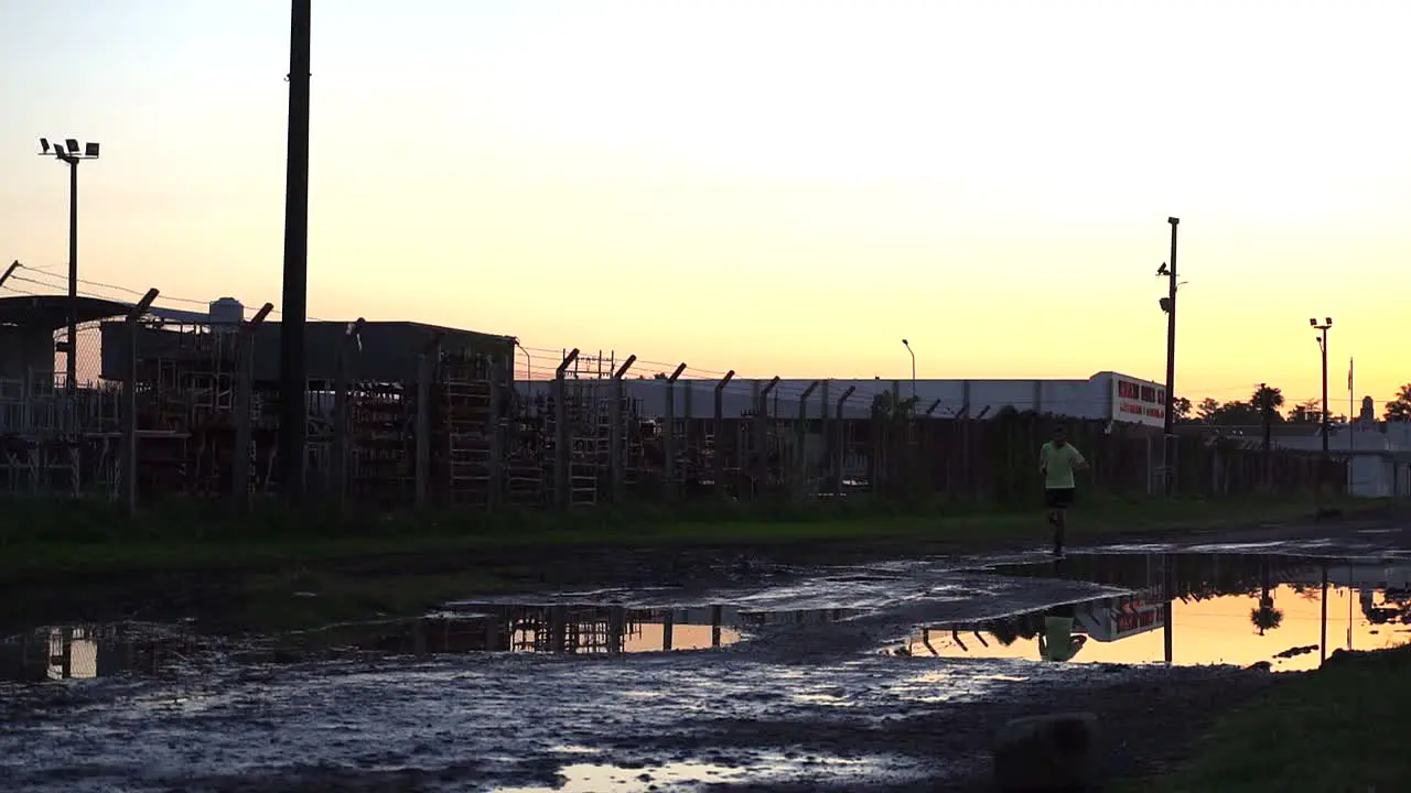 A lonely runner at dusk on a flooded service road beside a factory