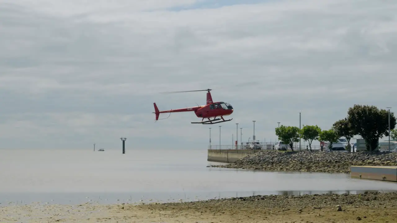 red helicopter landing in Cairns esplanade lagoon on a cloudy day at slow motion in queensland australia