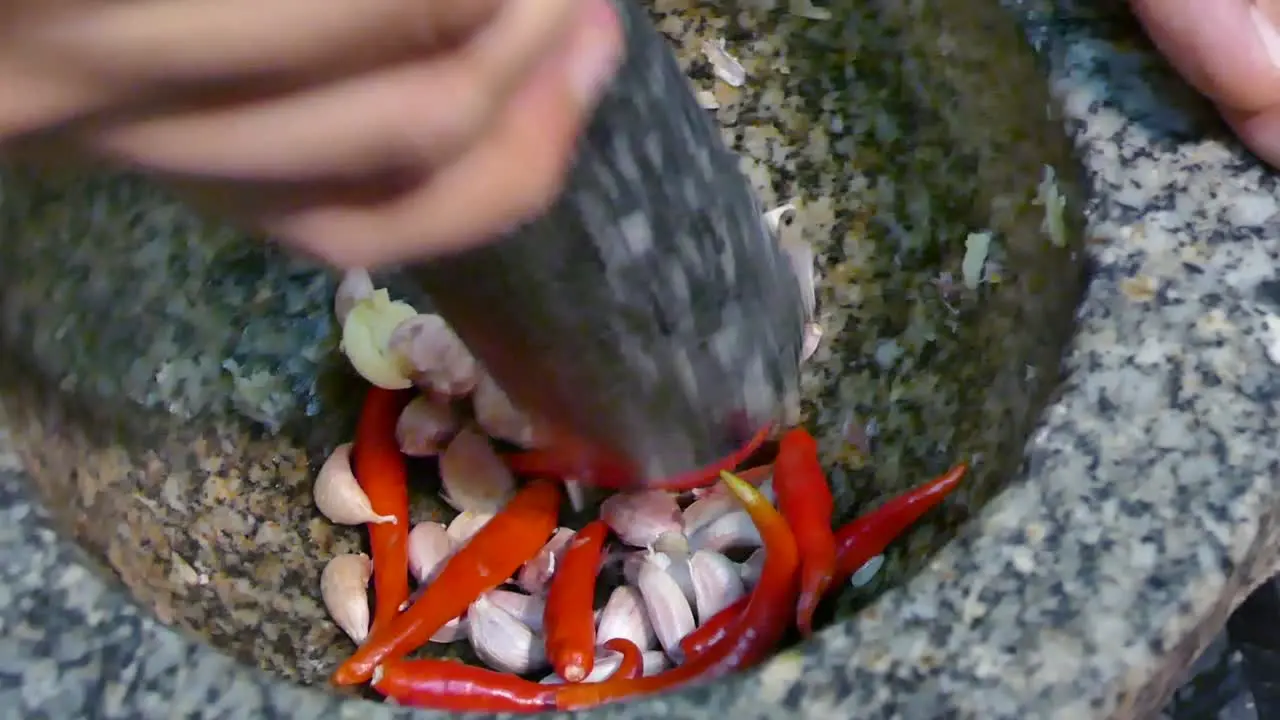 Asian Hand Using Stone Mortar and Pestle Crushing Garlic and Red Chili Pepper Close Up Slow-Motion