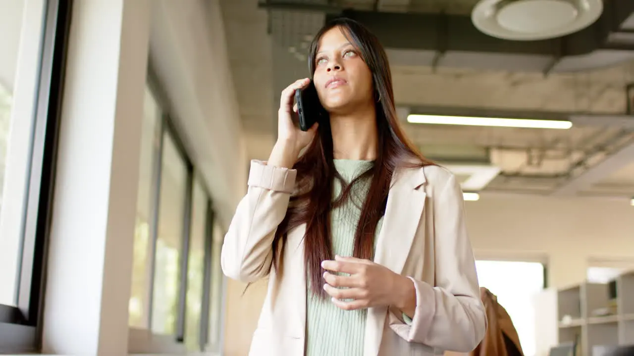 Happy biracial casual businesswoman talking on smartphone in office slow motion