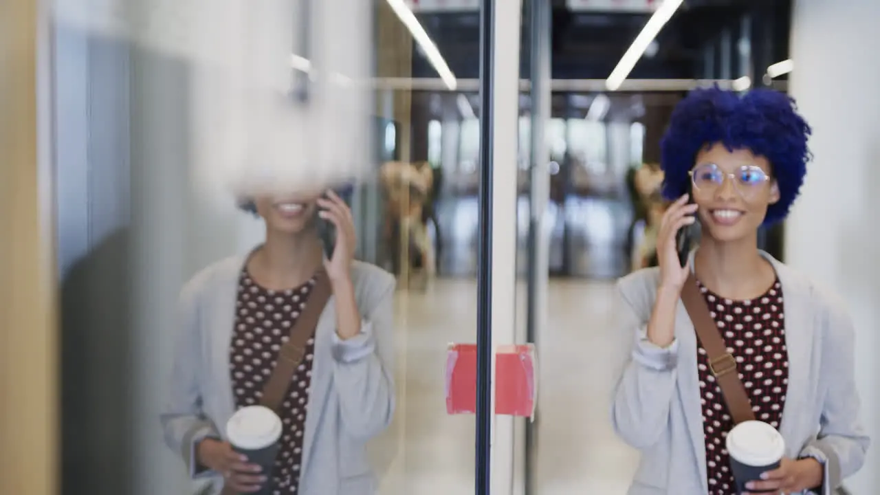 Biracial businesswoman with blue afro talking on smartphone in office slow motion