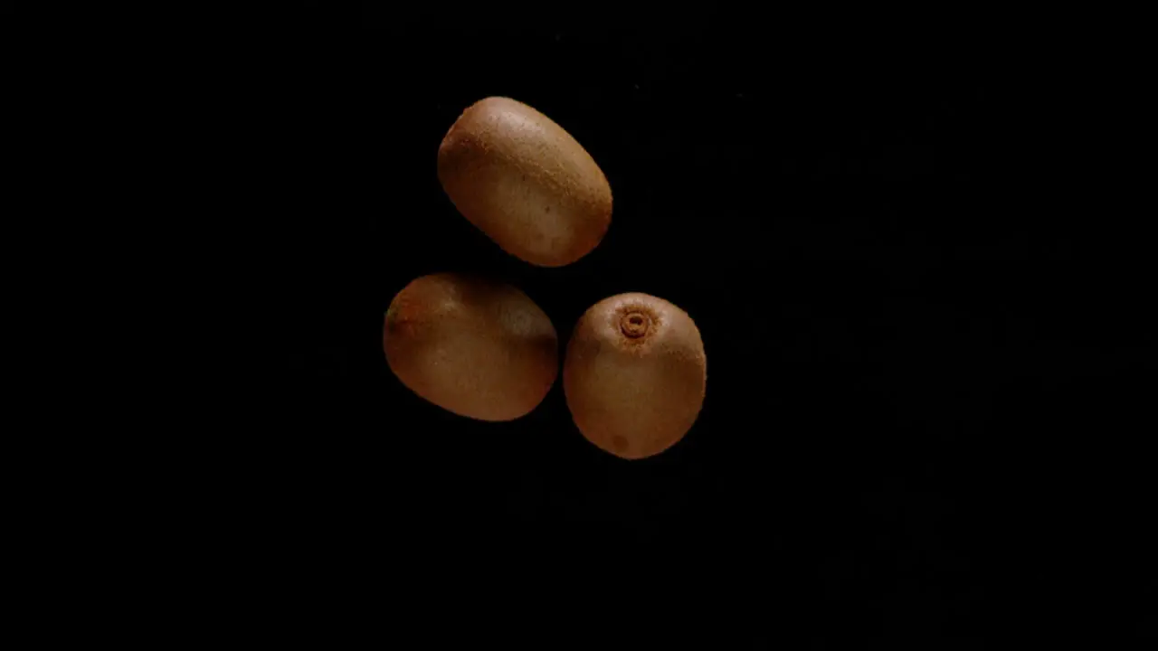 Bunch of kiwi fruit falling down isolated on black background super slow motion view