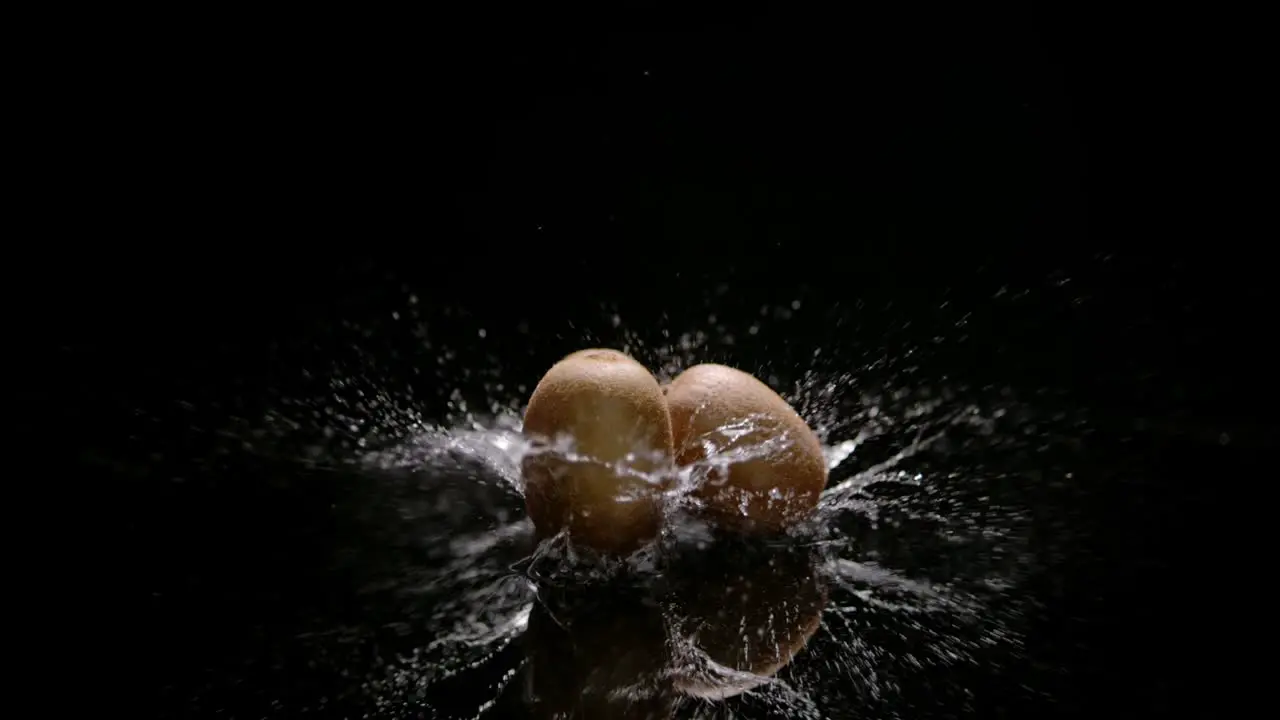 Kiwi fruits falling on water surface with huge splash isolated on black