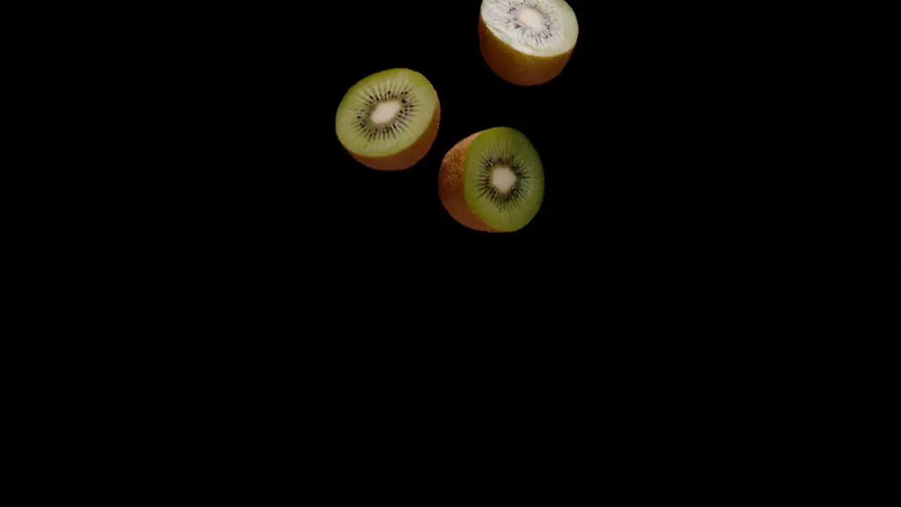 Cut in half kiwi fruit falling down isolated on black background slow motion