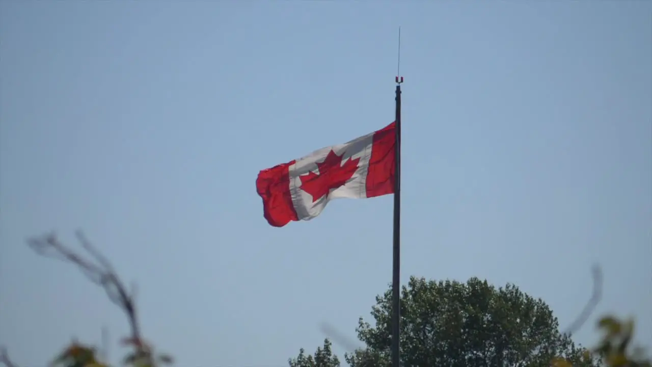 Canadian Flag On Pole Waving In The Wind Against Blue Sky