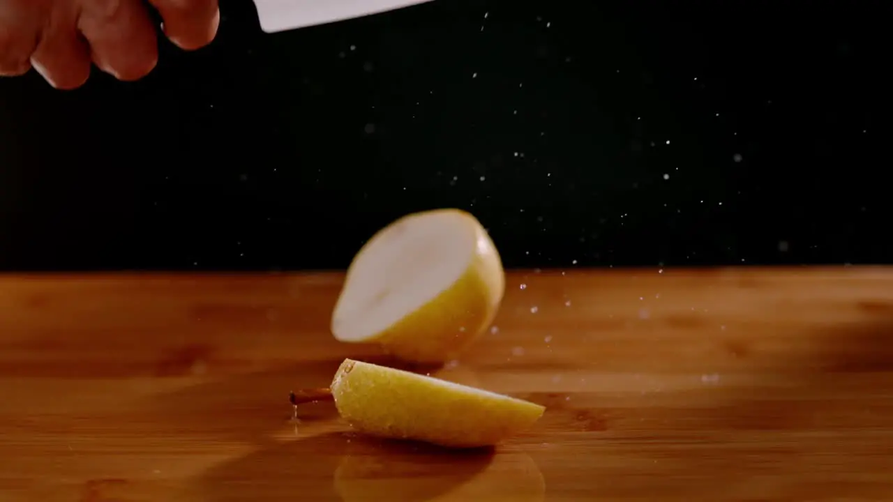 Sharp knife cutting wet pear with flying water drops on wooden board super slow motion