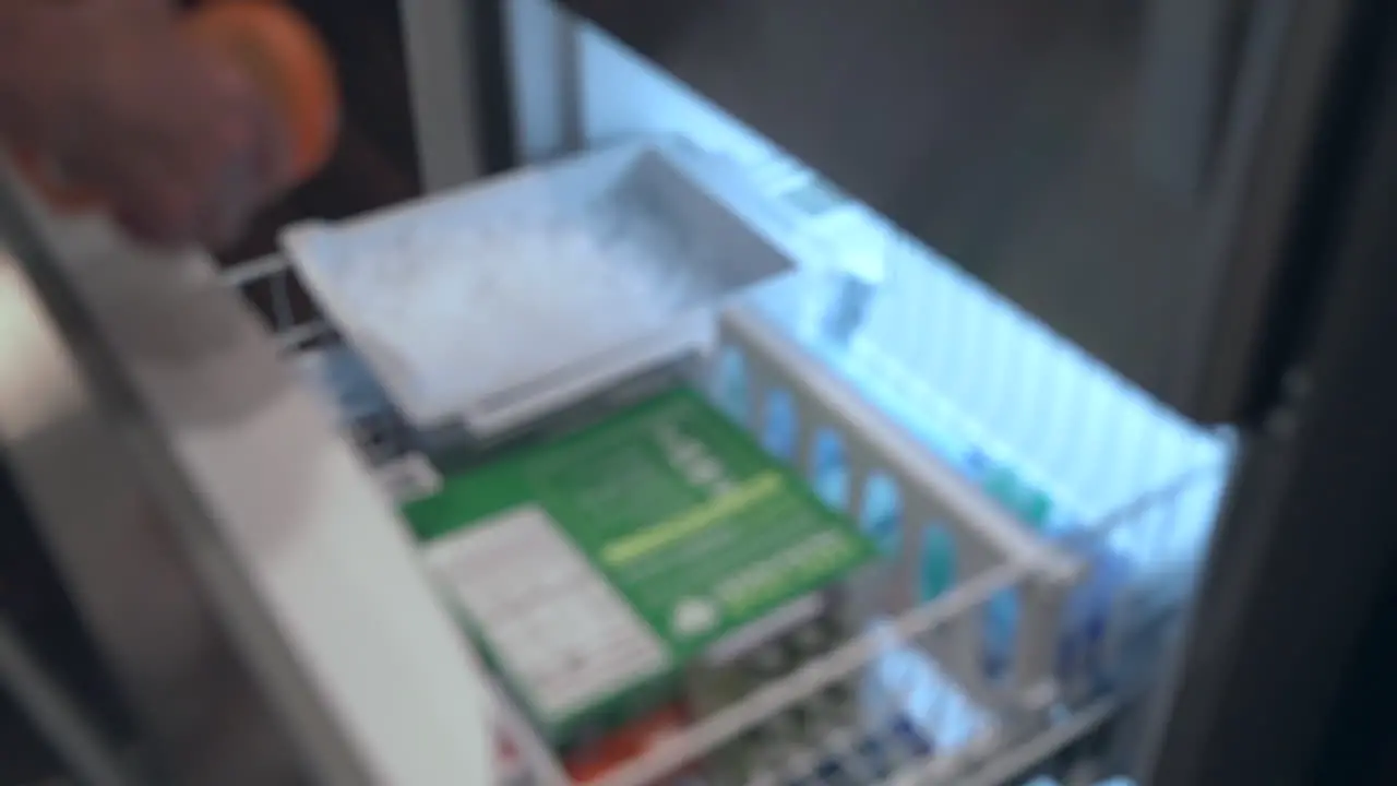 Slow motion out of focus shot of man reach into freezer to fill his supplement shaker with fresh ice appliance