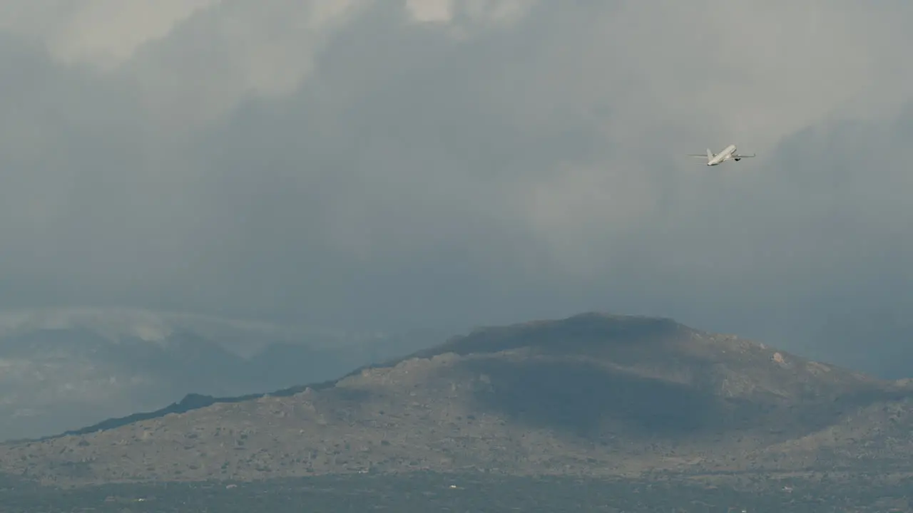 Aircraft gaining height and flying over mountains in cloudy sky