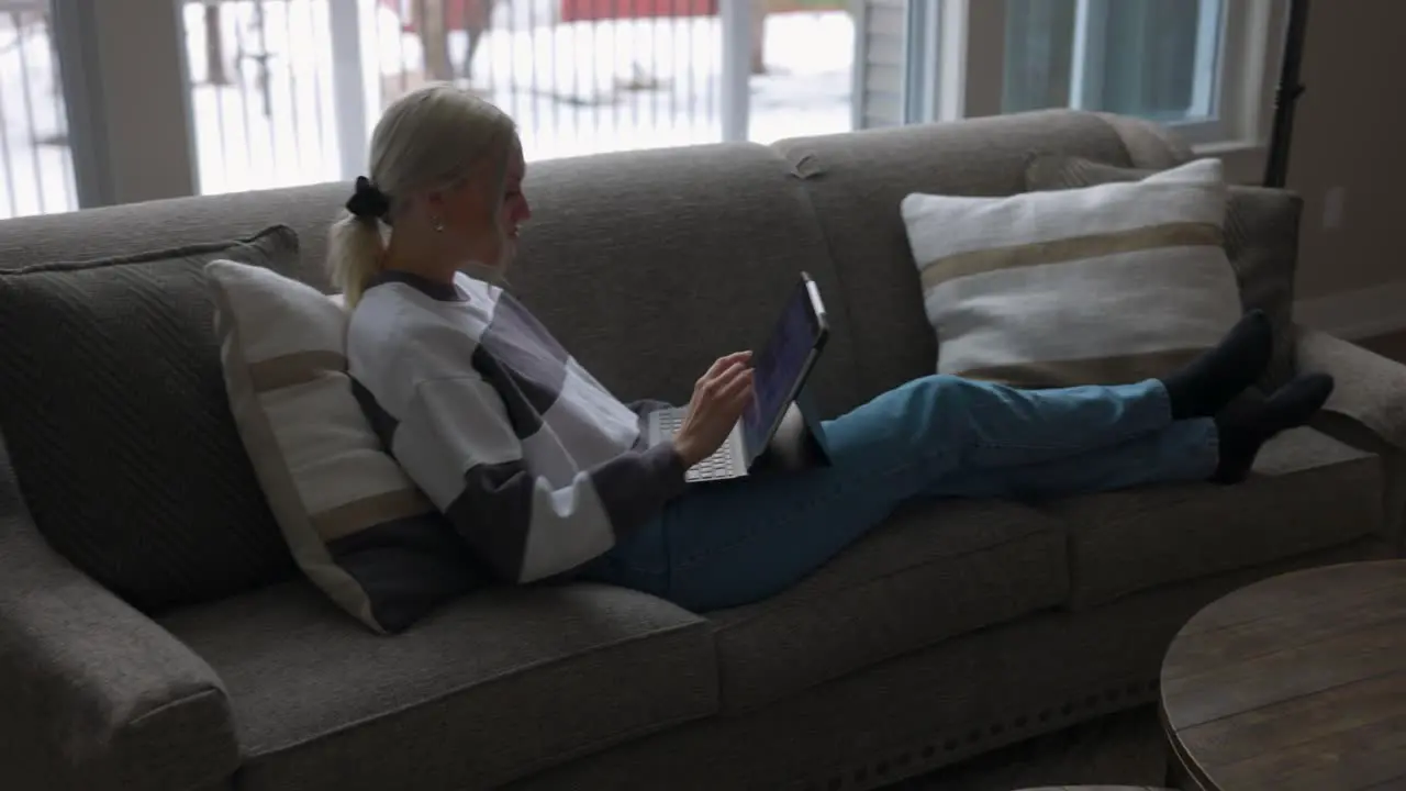 woman walking to the couch to lay down and scroll through tablet while drinking coffee in a nice house