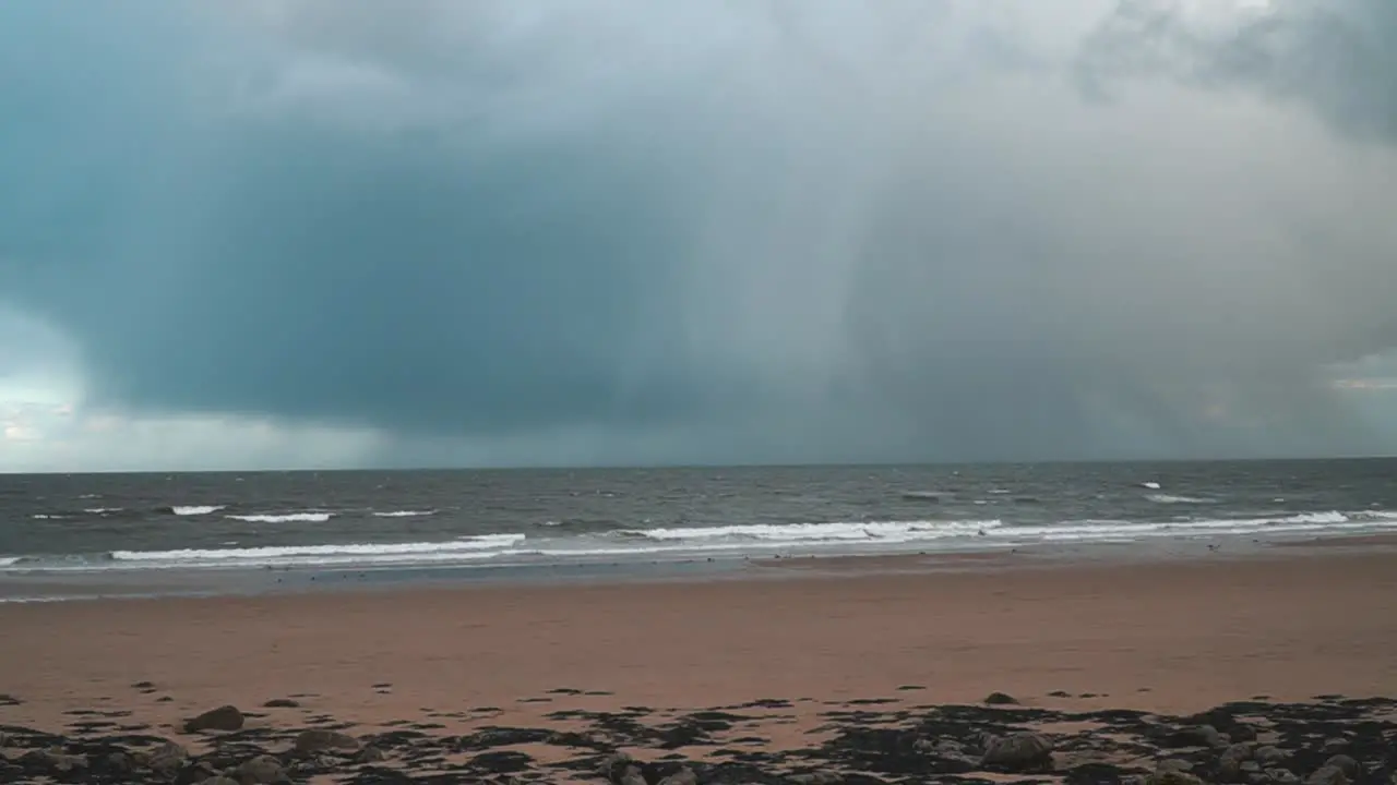 Timelapse of storm rain grey clouds raining over the ocean with waves crashing onto an empty beach in South Shields England