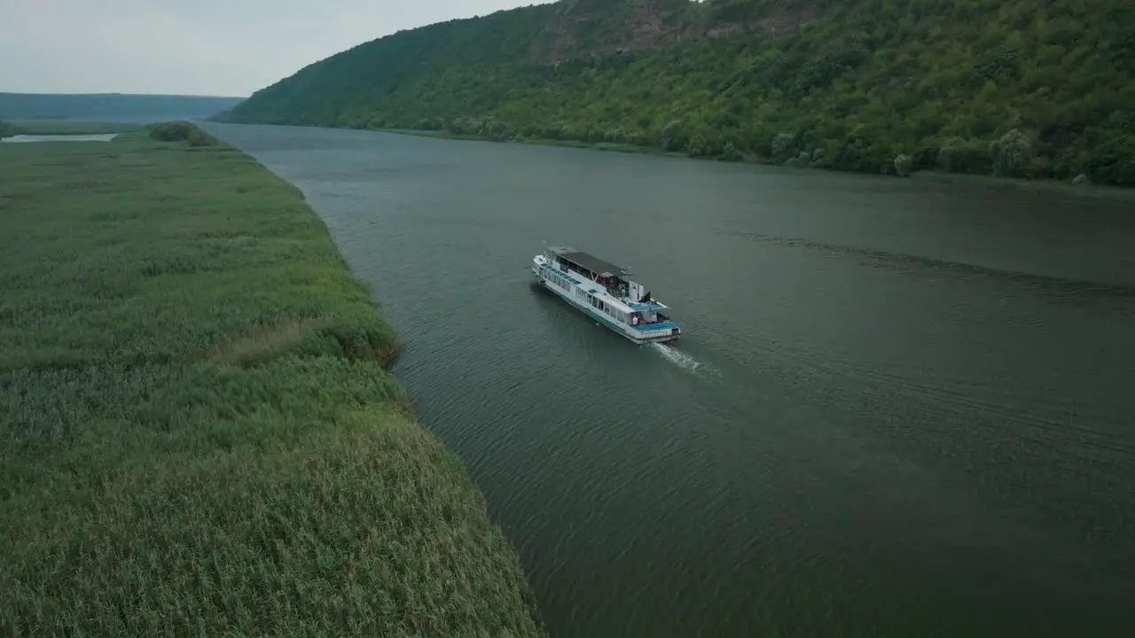 rlateral movement escort boat behind a boat that moves on a river next to tall grass through high mountains to the side horizon