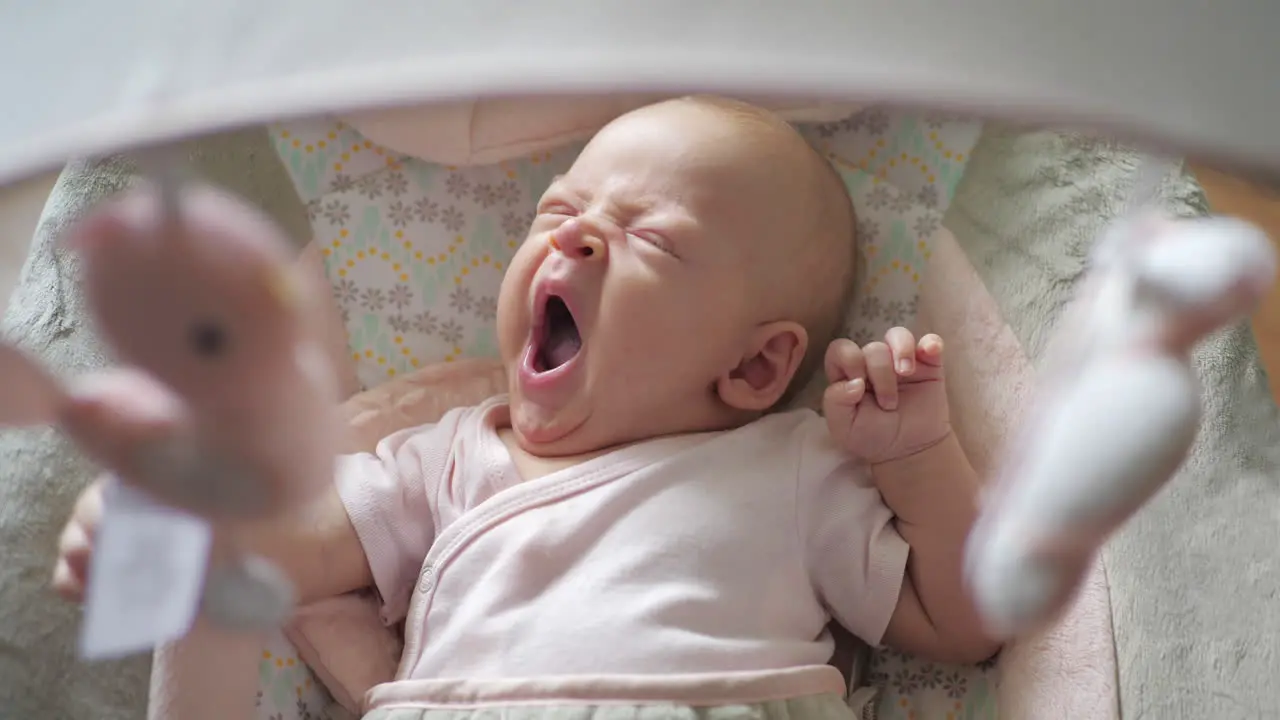 Yawning baby girl in child rocker with toys