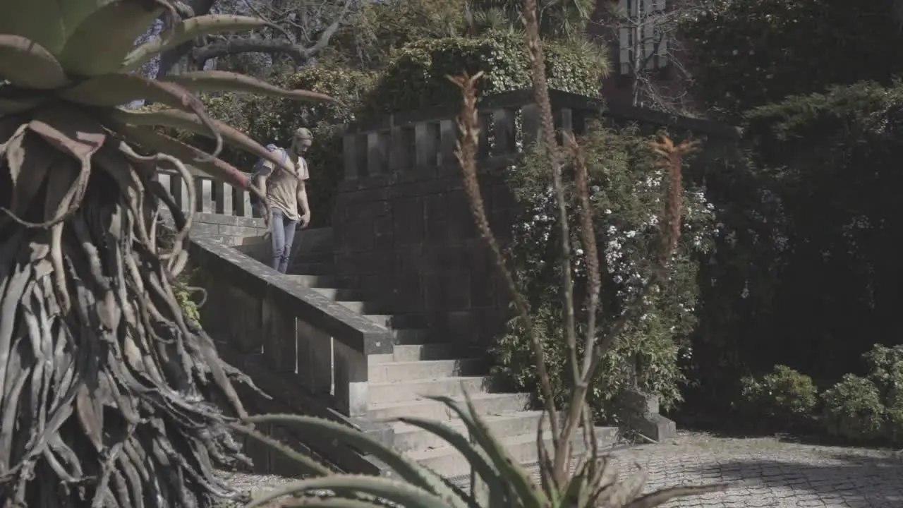 Traveler with backpack walking down the stairs in public park summer Oporto Spain static shot