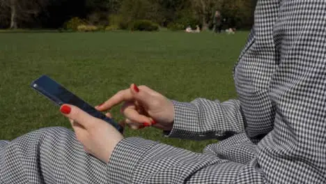 Medium Side Profile Shot of Female Hands Using Mobile Phone In Park