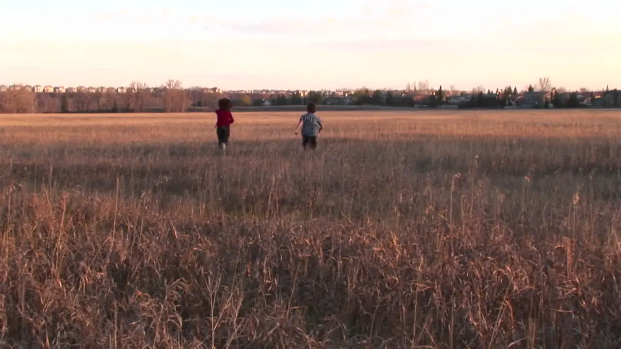 Medium shot of a boy and girl run freely out into an open field