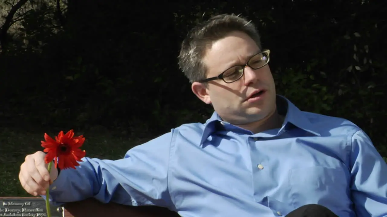 A man sits alone on a park bench while he holds two flowers