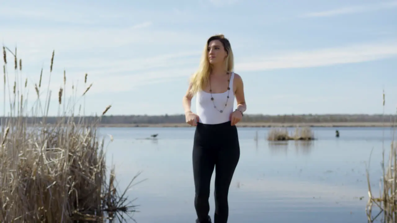 Confident trendy young woman walks towards the camera lake in the background