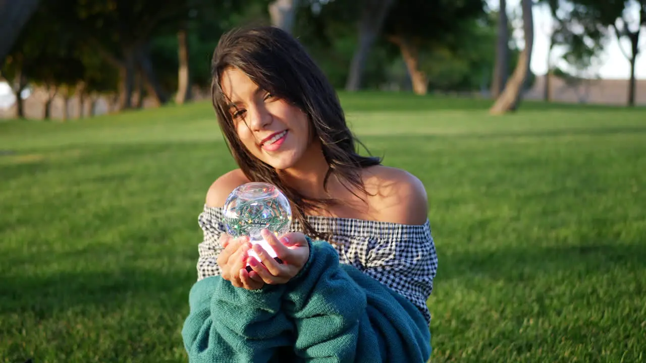 A cute young hispanic woman smiling happily in a park with a magic crystal ball